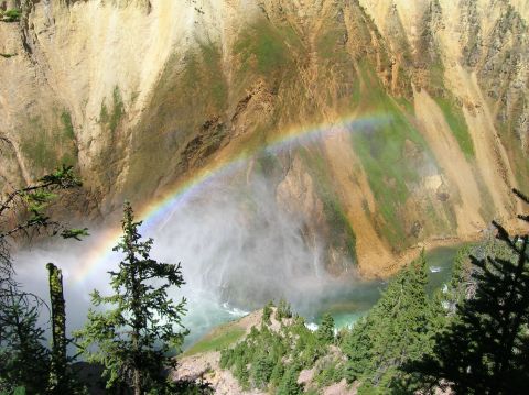 1996 Ford Bronco - A rainbow arcs over a misty waterfall cascading into a turquoise river, framed by steep, verdant canyon walls and evergreen trees.