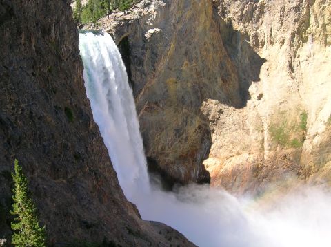 1996 Ford Bronco - A powerful waterfall cascades down a rocky canyon, creating a mist at its base where a faint rainbow is visible. Lush green trees grow on t…