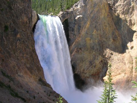 1996 Ford Bronco - A powerful waterfall cascades down a rocky canyon under a bright blue sky. Lush green trees line the top of the canyon walls.