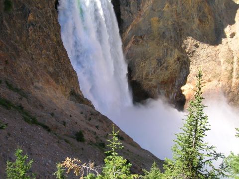 1996 Ford Bronco - A powerful waterfall cascades down a rocky cliff face, creating a large cloud of mist at its base. Evergreen trees are visible in the foreg…