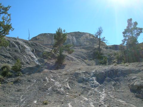 1996 Ford Bronco - A wide shot of a rocky, barren landscape with sparse trees under a bright blue sky. The terrain shows signs of mineral deposits and erosion…