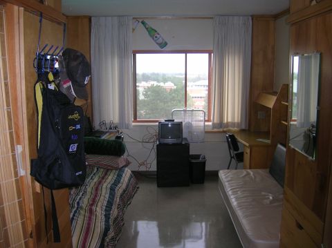1996 Ford Bronco - This is a cluttered dorm room with a bed, desk, and window. A backpack and hats hang on a rack near the door.