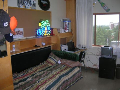1996 Ford Bronco - This image shows a dorm room with a bed, desk, and various decorations. A neon Corona sign is prominently displayed above a shelf.