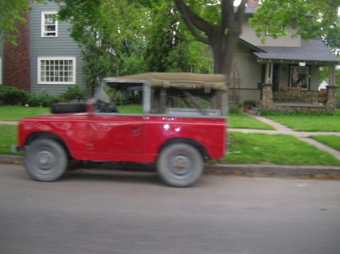 1996 Ford Bronco - A red, soft-top, vintage SUV is parked on the side of a residential street. The vehicle is positioned in front of a house with a well-maint…