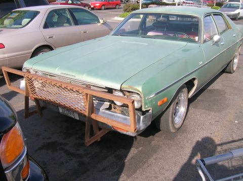 1996 Ford Bronco - A light green, four-door sedan with a custom metal grille guard is parked in a lot. The car has chrome wheels and a visible license plate.