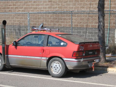 1996 Ford Bronco - A red Honda CRX with a large vertical exhaust pipe on the driver's side and train horns mounted on the roof rack.