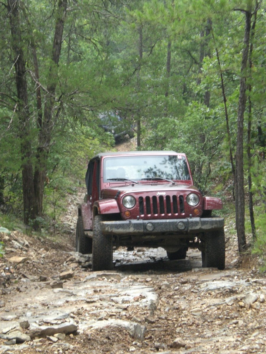 Red Jeep Wrangler driving on a rocky forest trail.