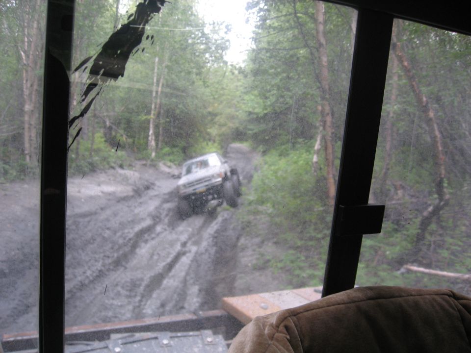 White Ford F-250 driving on a muddy forest trail, seen through a dirty windshield.