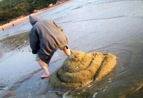 1992 Ford Mustang - A person wearing a grey hooded sweatshirt and shorts is standing on a beach, with their right leg extended towards a large pile of sand tha…