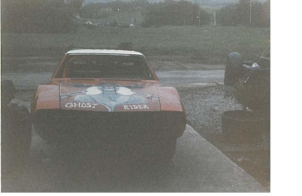 Red car with white roof and "GHOST RIDER" text on hood, front view.