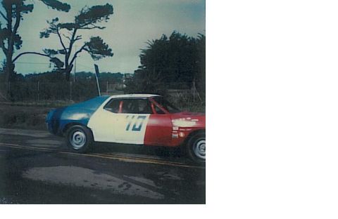 1991 Ford Bronco - A race car with a blue rear, white middle, and red front is driving on a wet asphalt road. The car has the number "10" in blue on its side.