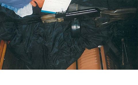 1991 Ford Bronco - The image shows a firearm with a drum magazine resting on a black fabric. A document with text is partially visible near the firearm.
