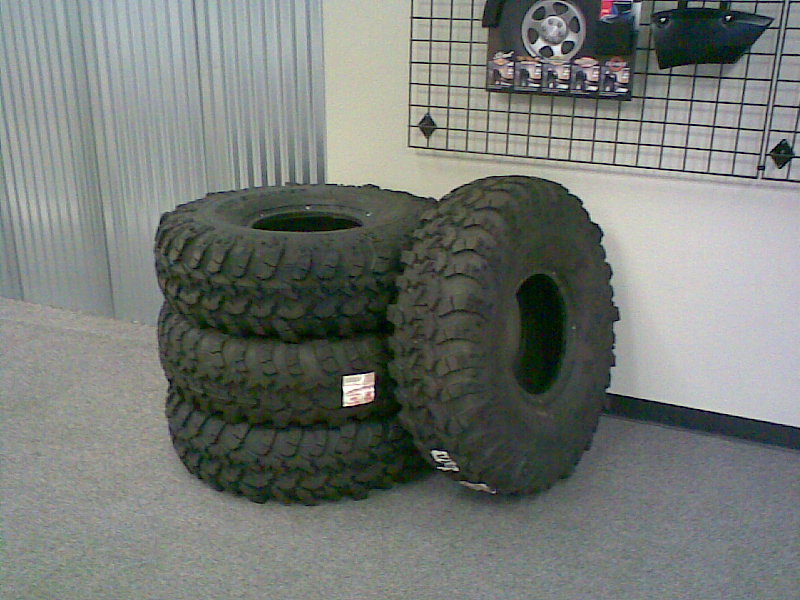 Four large off-road tires stacked in a display.