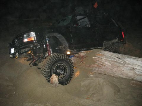 1996 Ford Bronco - A black Ford Bronco is stuck in the sand, with its front tire resting against a large fallen log. The vehicle appears to be modified for of…