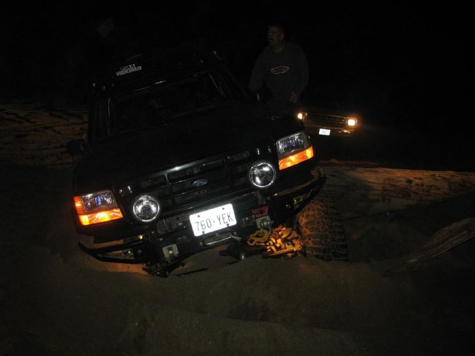 Black 1996 Ford Bronco stuck in sand at night.