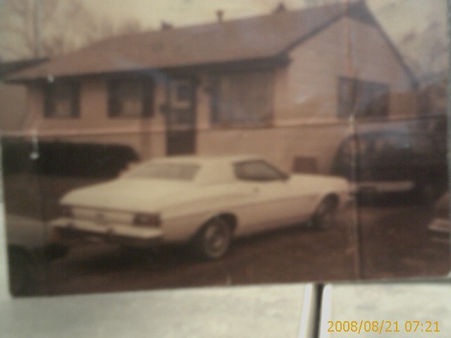 White coupe parked in front of a house, rear three-quarter view.