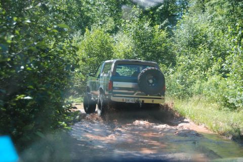 1996 Ford Bronco - Photograph of a teal Ford Bronco on a wooded mud trail, not a technical document.