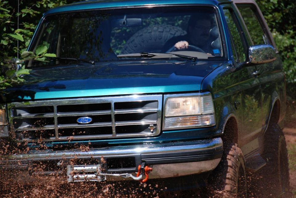 Teal Ford Bronco front end splashing mud with winch