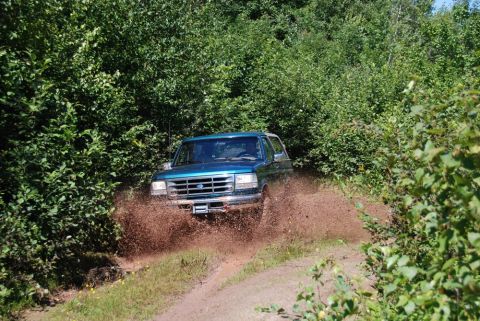 1996 Ford Bronco - Photograph of a teal Ford Bronco spraying mud on a forest trail, not a technical document.