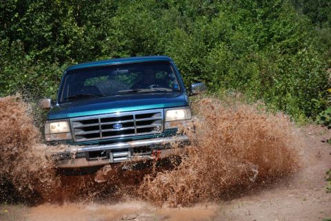 1996 Ford Bronco - Photograph of a teal Ford truck plowing through deep mud, not a technical document.