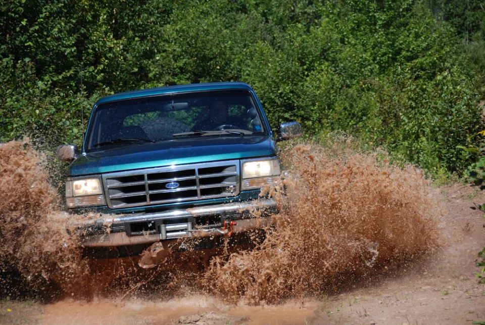 Teal Ford truck blasting through a large mud puddle