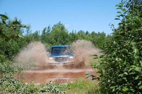 1996 Ford Bronco - Photograph of a blue Ford truck spraying mud under a clear sky, not a technical document.
