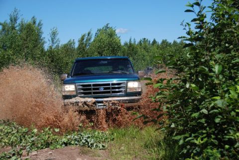 1996 Ford Bronco - Photograph of a teal Ford truck throwing mud off-road, not a technical document.