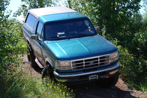 1996 Ford Bronco - Photograph of a mud-covered teal Ford Bronco on a trail, not a technical document.