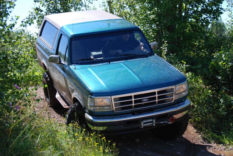 Muddy teal Ford Bronco with topper on a forest trail