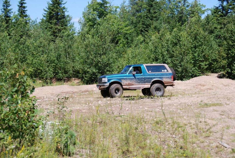 Teal Ford Bronco parked on a dirt clearing in the woods