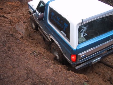 1989 Ford Bronco - This Ford Bronco is navigating a muddy, off-road trail, with its tires sunk deep into the dirt.