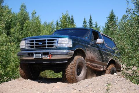 1996 Ford Bronco - 1996 Ford Bronco navigating an off-road trail with muddy tires and body.
