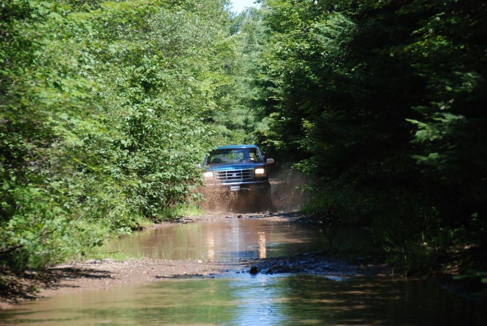 1996 Ford Bronco driving through mud on a wooded trail
