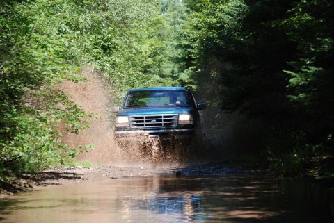 1996 Ford Bronco - Photograph of a teal Ford truck fording a muddy puddle, not a technical document.