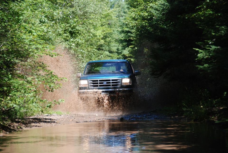 Teal Ford truck driving through a long muddy water puddle