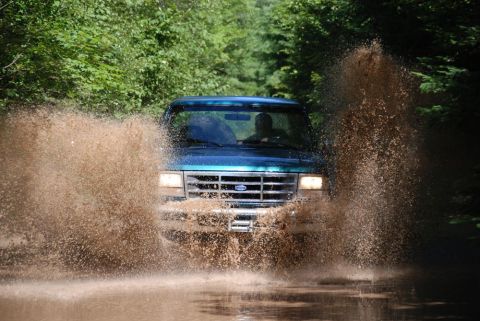 1996 Ford Bronco - Photograph of a teal Ford truck spraying mud through water, not a technical document.