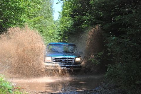 1996 Ford Bronco - Photograph of a blue Ford truck plowing through a mud puddle, not a technical document.
