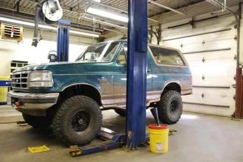1996 Ford Bronco - Photograph of a 1990s Ford Bronco raised on a two-post hoist in a service garage, not a technical document.