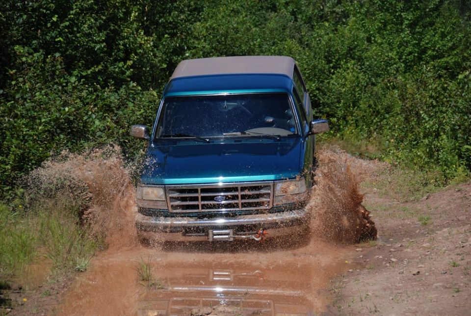 Blue Ford truck with camper splashing through a muddy trail
