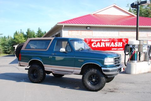 1996 Ford Bronco - Photograph of a lifted teal Ford Bronco parked outside a self-serve car wash, not a technical document.