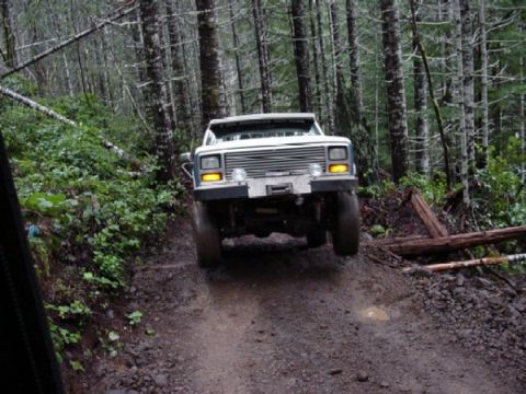 1989 Ford Bronco - A white SUV navigates a challenging muddy path through a dense forest.