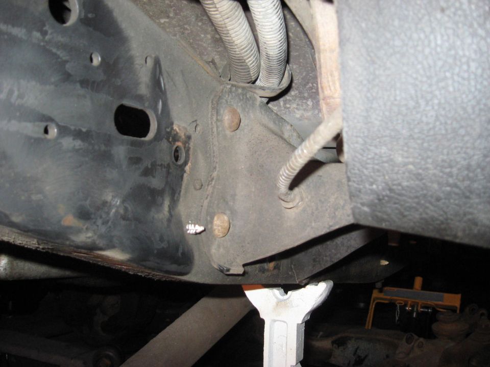 Underside of a vehicle frame with wiring and jack stands.