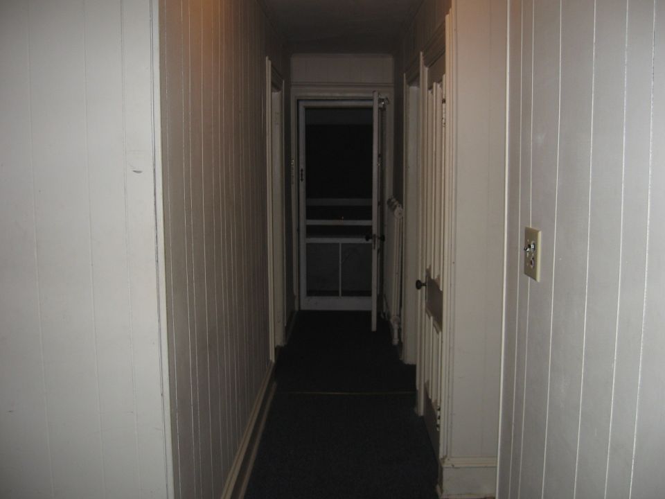 Interior hallway with paneled walls and a screen door at the end.