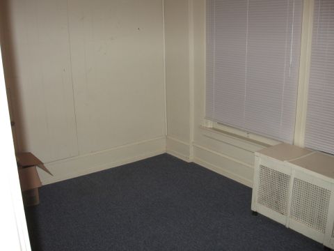 1984 Ford Bronco - This is an empty room with blue carpet, a window with blinds, and a heating unit. There is a cardboard box in the corner.
