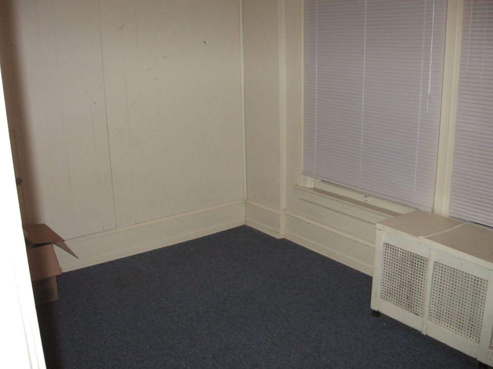 Empty room with blue carpet, window, heating unit, and cardboard box.
