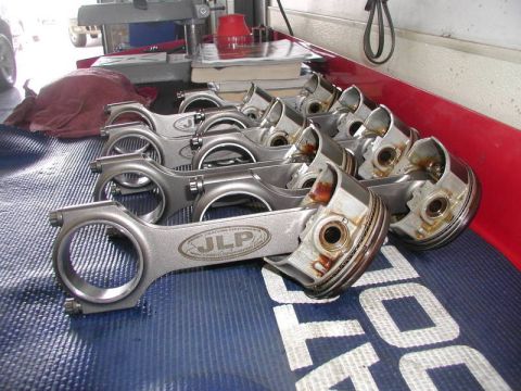 2007 Ford Mustang - Photograph of JLP forged connecting rods and pistons displayed on a bench, a physical-parts photo not a document.