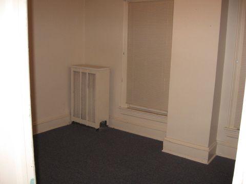 1984 Ford Bronco - An empty room with dark carpet, a white radiator cover, and a window with blinds.