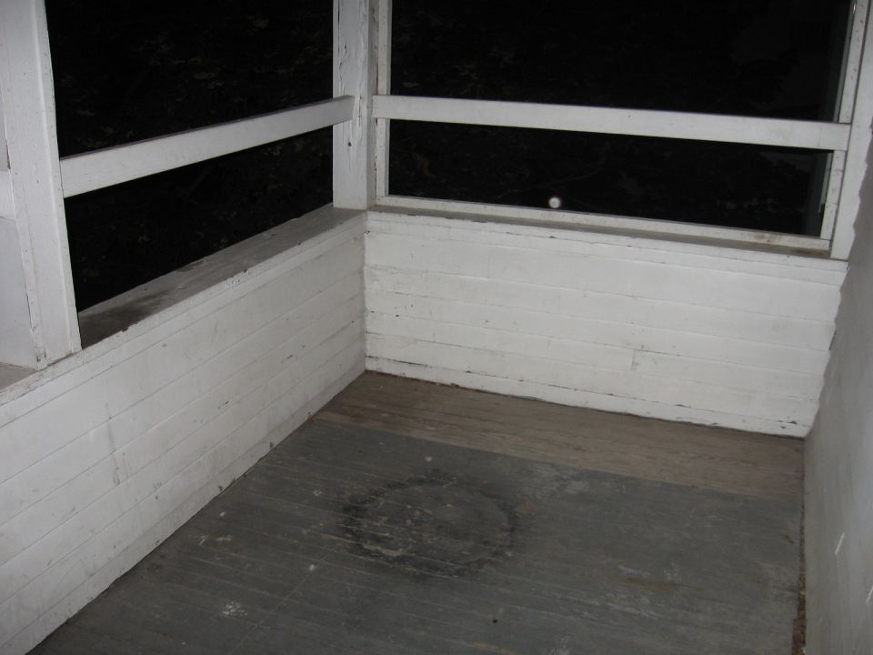 Interior corner of a wooden porch with white painted railings and walls, dark background visible through openings