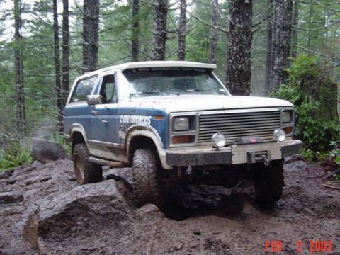 1989 Ford Bronco - Ford Bronco navigating a challenging, muddy off-road course in a wooded area.