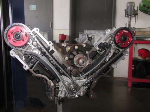 2007 Ford Mustang - A V8 engine is disassembled, showing its internal timing chain mechanism and red cam gears.